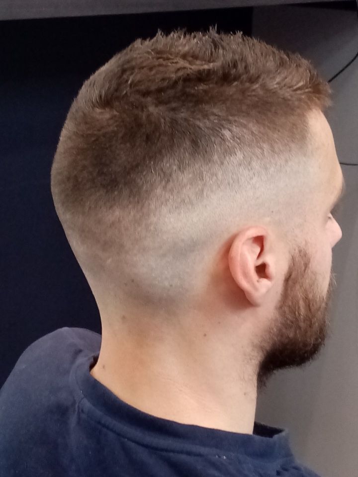 Homme avec une coupe de cheveux décolorée et une barbe de côté, avec des cheveux foncés sur le dessus et un décolleté rasé.