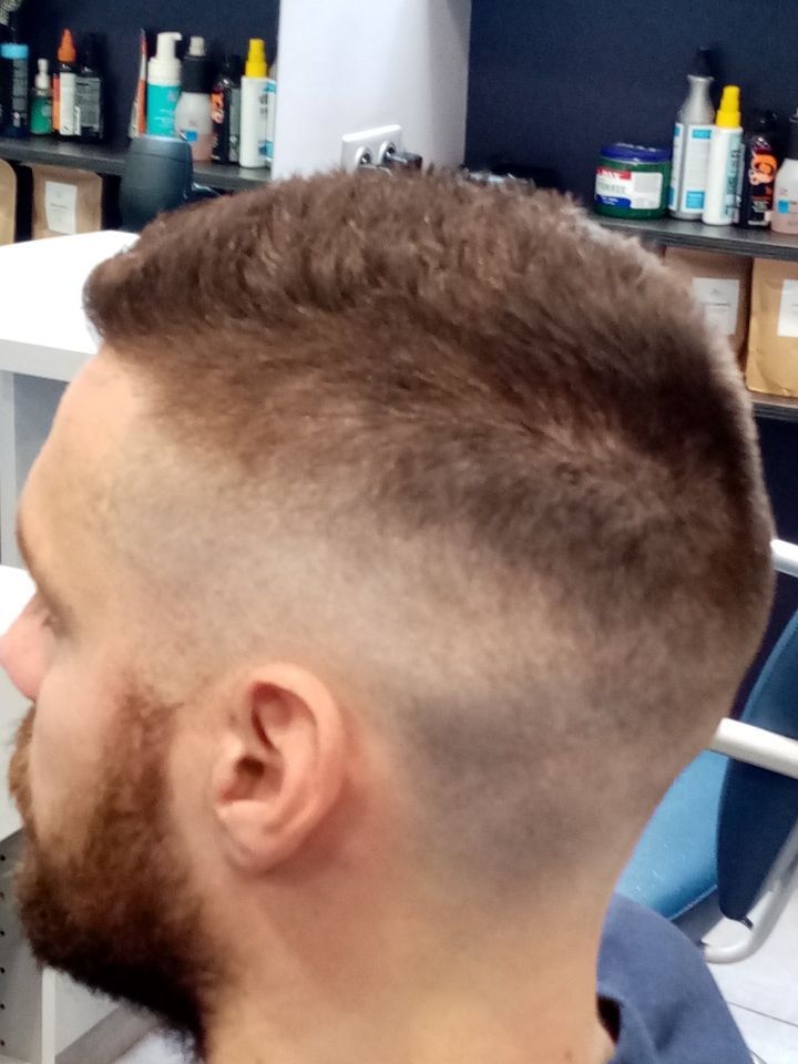 Homme avec coupe de cheveux décolorée et barbe complète, vue de profil.