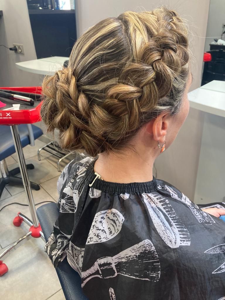 Femme avec une coiffure chignon tressée dans un salon, portant une cape à motifs noirs et blancs.