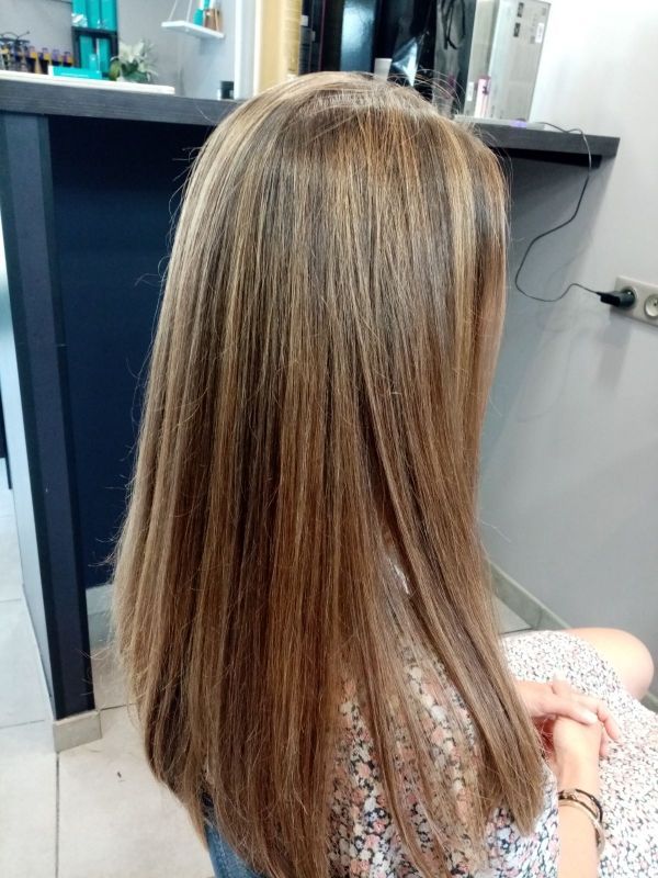 Cheveux longs et raides d'une femme avec des mèches blondes dans un salon, assise, les mains jointes.