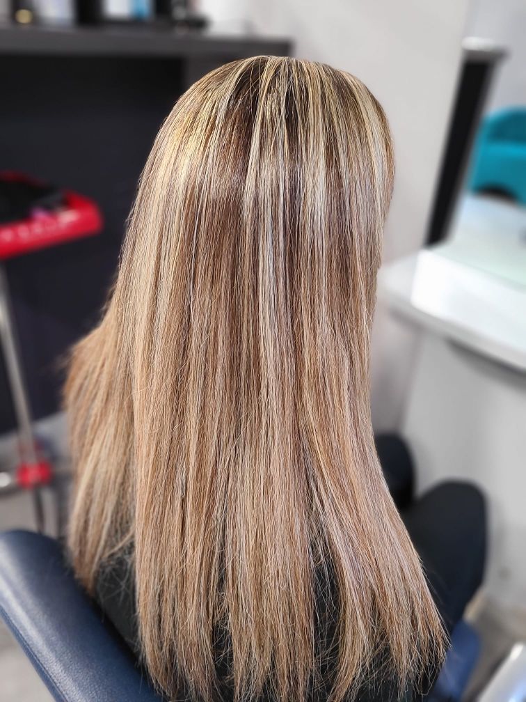 Femme aux cheveux longs et méchés blonds et bruns, assise sur une chaise de salon.