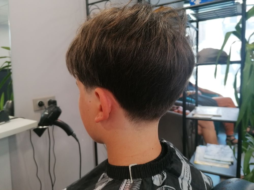 Une personne aux cheveux courts et foncés, avec une légère décoloration sur le cou. Assise dans un salon de coiffure.