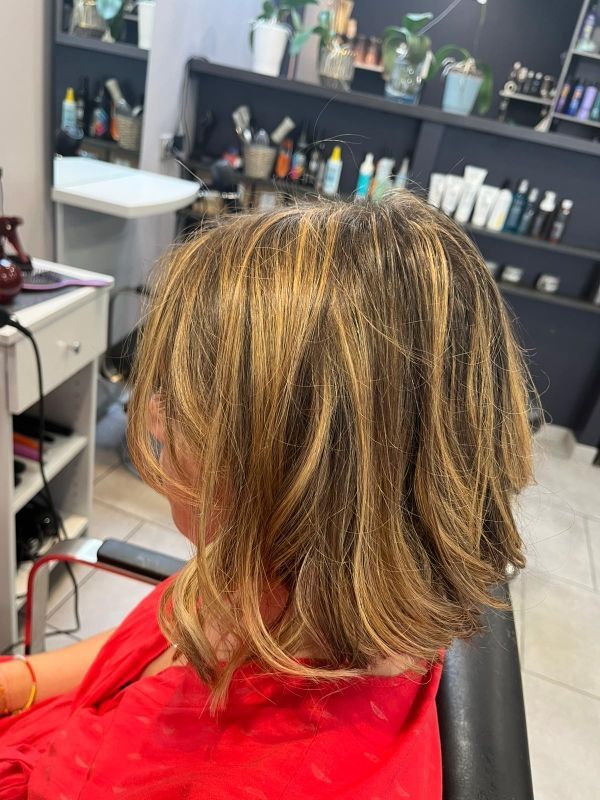 Femme aux cheveux bruns méchés dans un fauteuil de salon, portant un haut rouge.