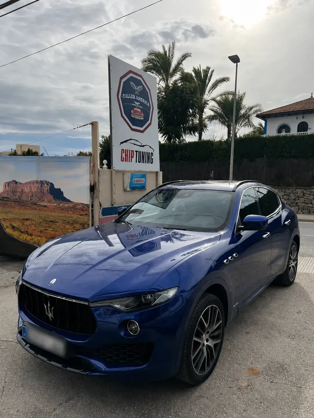 Un SUV Maserati azul estacionado al aire libre cerca de un letrero