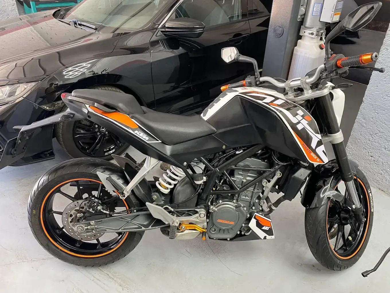 Motocicleta deportiva negra y naranja estacionada en un garaje junto a un coche negro.