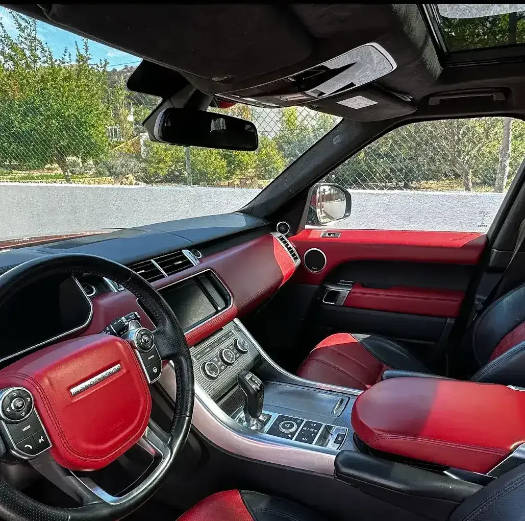 Interior de un coche de lujo con asientos, salpicadero y consola central de cuero rojo a la luz del día.
