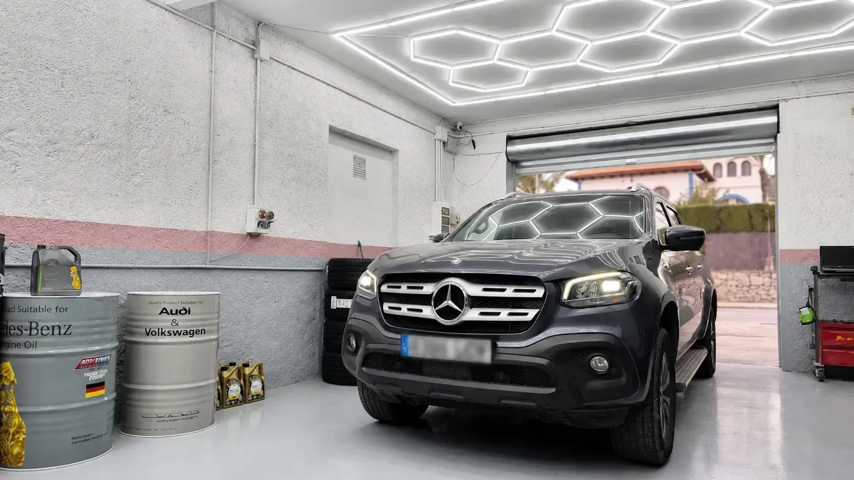 Un SUV Mercedes negro estacionado dentro de un luminoso garaje residencial con luces de techo hexagonales.