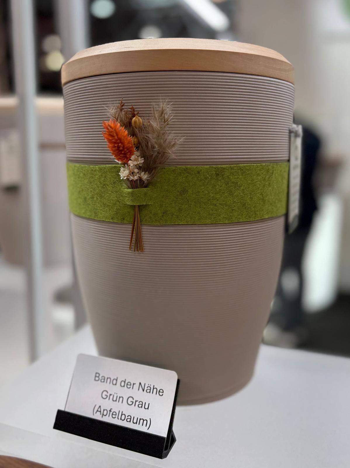 Decorated gray vase with green band and dried flowers, displayed beside a small label.