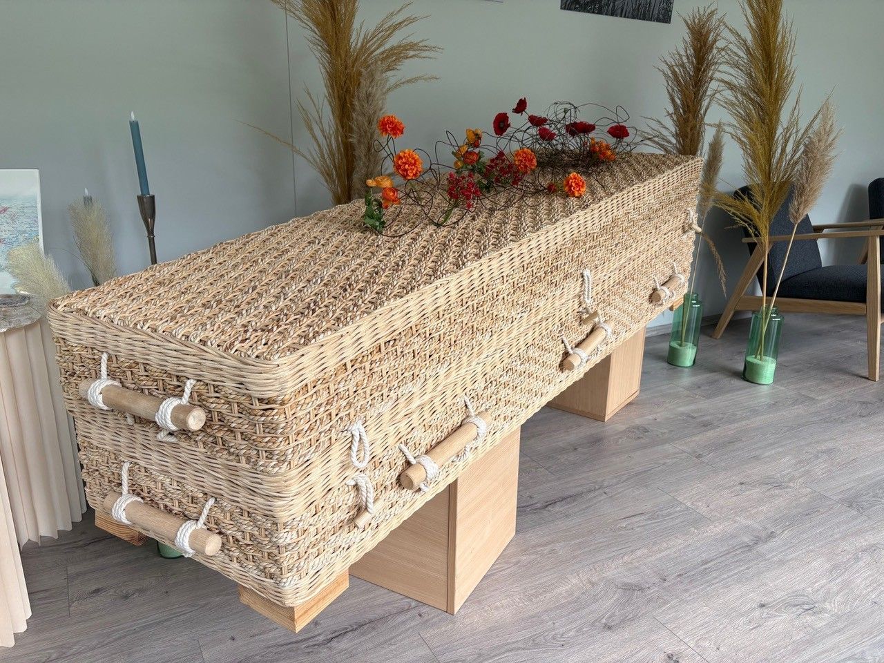 Ein sargähnlicher Tisch aus geflochtenem Korbgeflecht mit Blumen und getrockneten Gräsern in einem modernen Raum