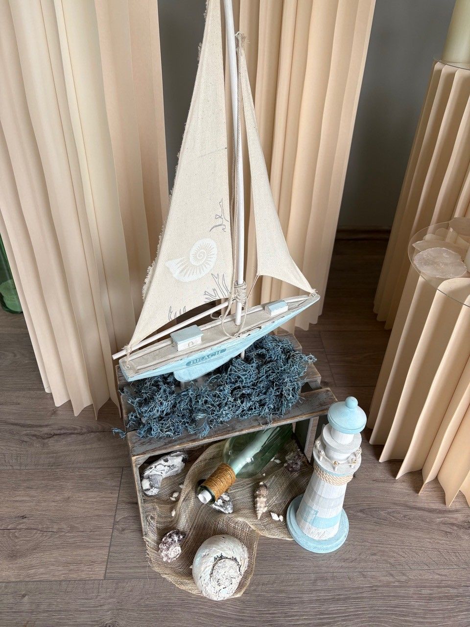Dekoratives weißes Segelboot auf einem Regal mit Muscheln und einer Leuchtturmfigur