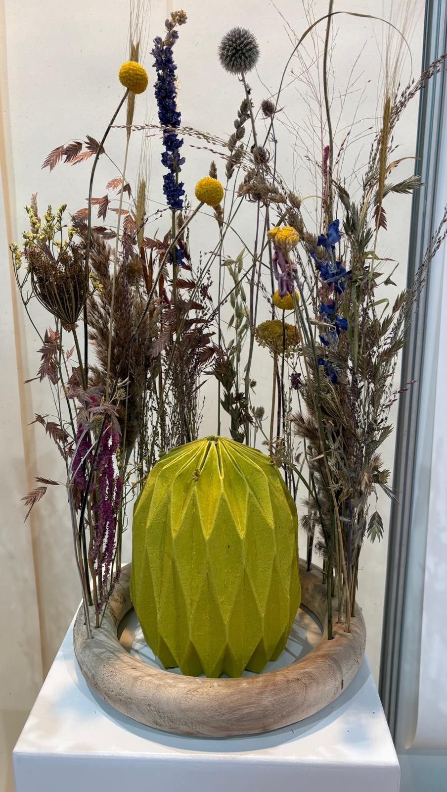 Green faceted candle centerpiece in a glass bowl with dried flowers and seed heads