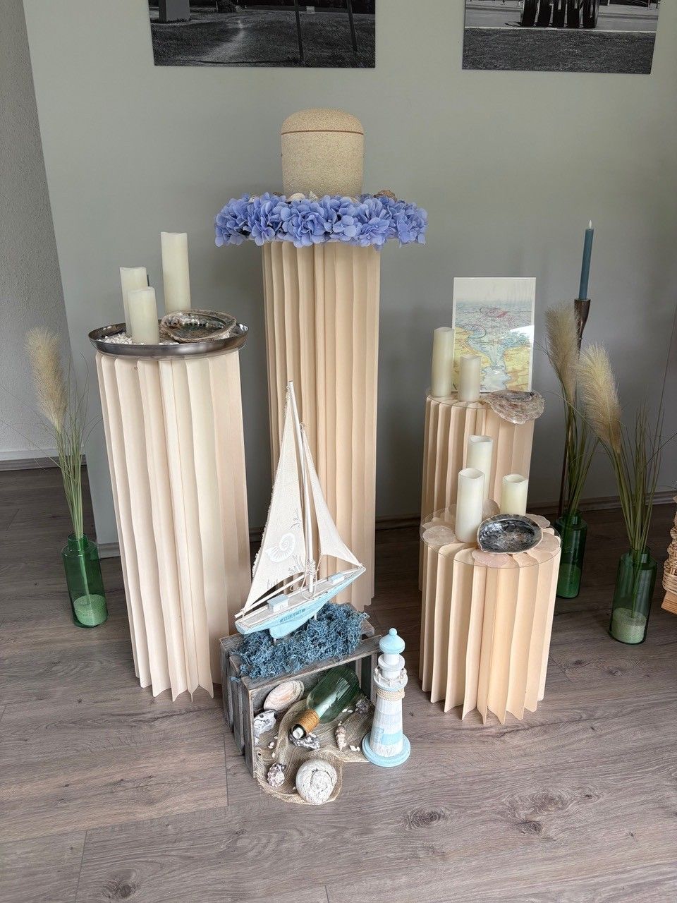 Dekorative Küstenkulisse mit Treibholzsockeln, Segelboot, Muscheln und blauen Blumen auf einem Holzboden