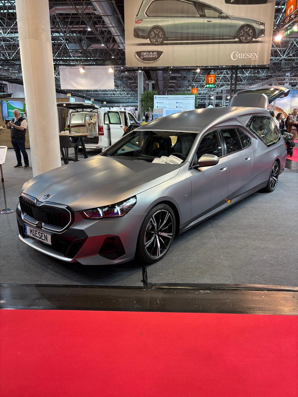Silver BMW sedan on display at an indoor auto show with a red carpet foreground