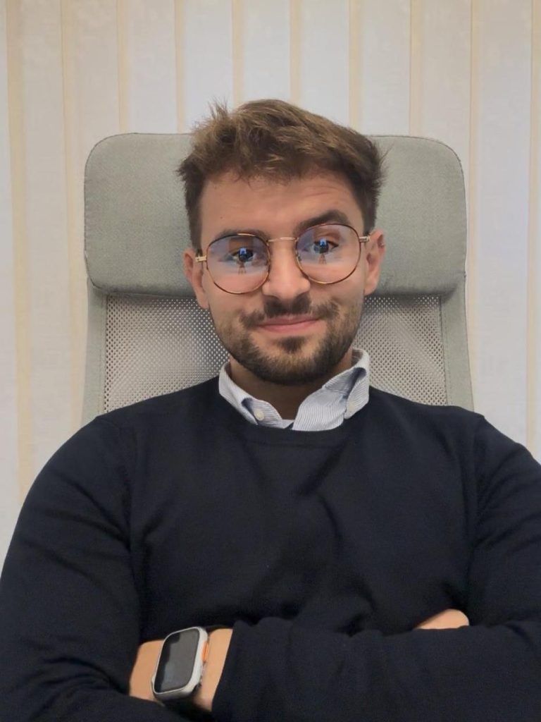 Hombre con gafas y suéter azul marino se sienta con los brazos cruzados; en el interior.