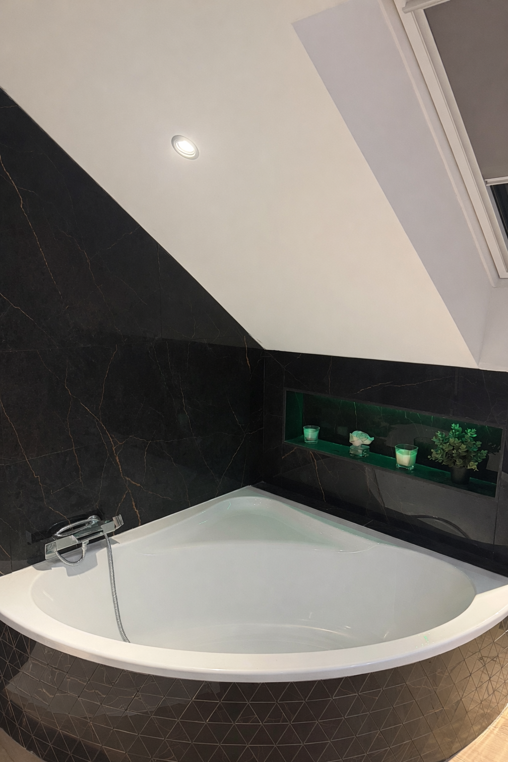 Une personne en combinaison grise et gants installe des carreaux de marbre blanc dans une douche, à côté d'accessoires de douche en cuivre.