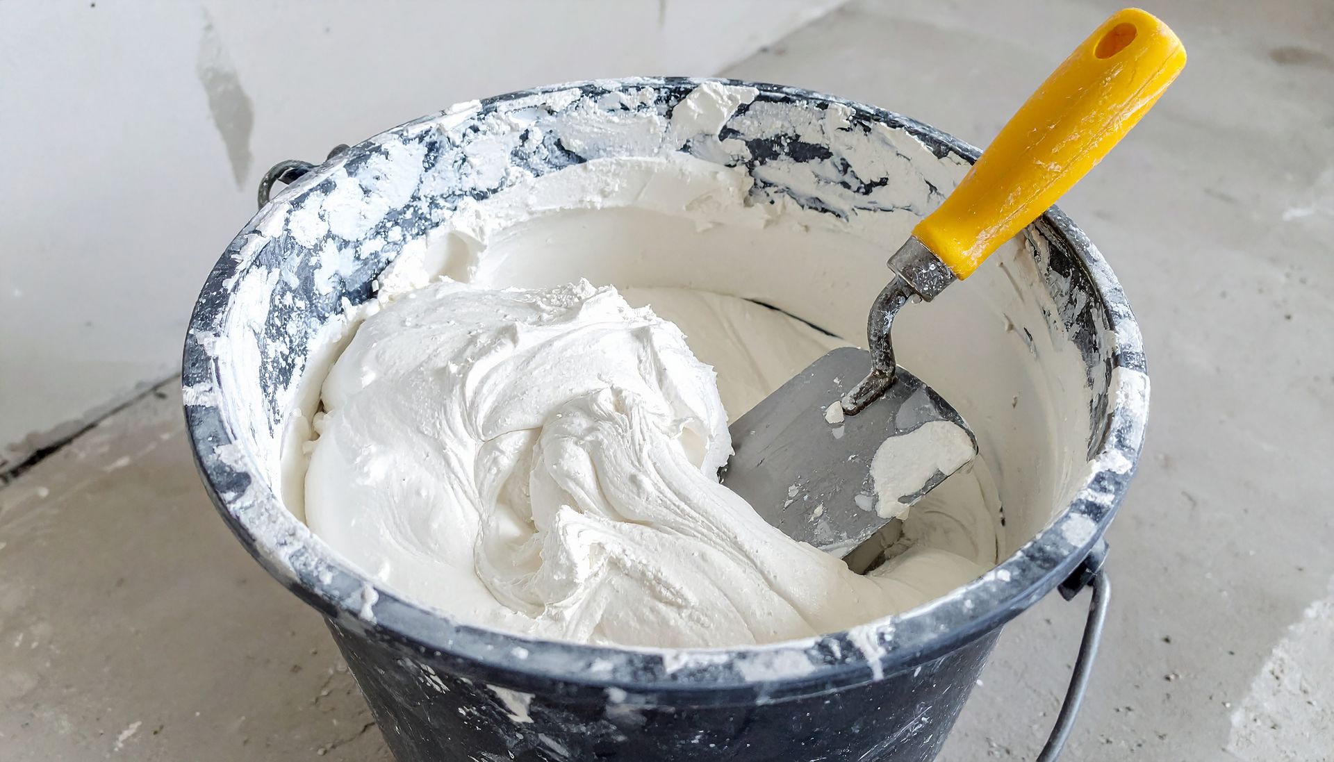 Seau d'enduit à joints blanc avec une truelle, sur un chantier.