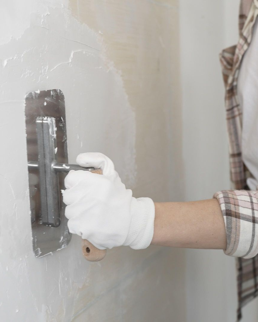 Personne portant des gants et utilisant une truelle pour appliquer du plâtre sur un mur.