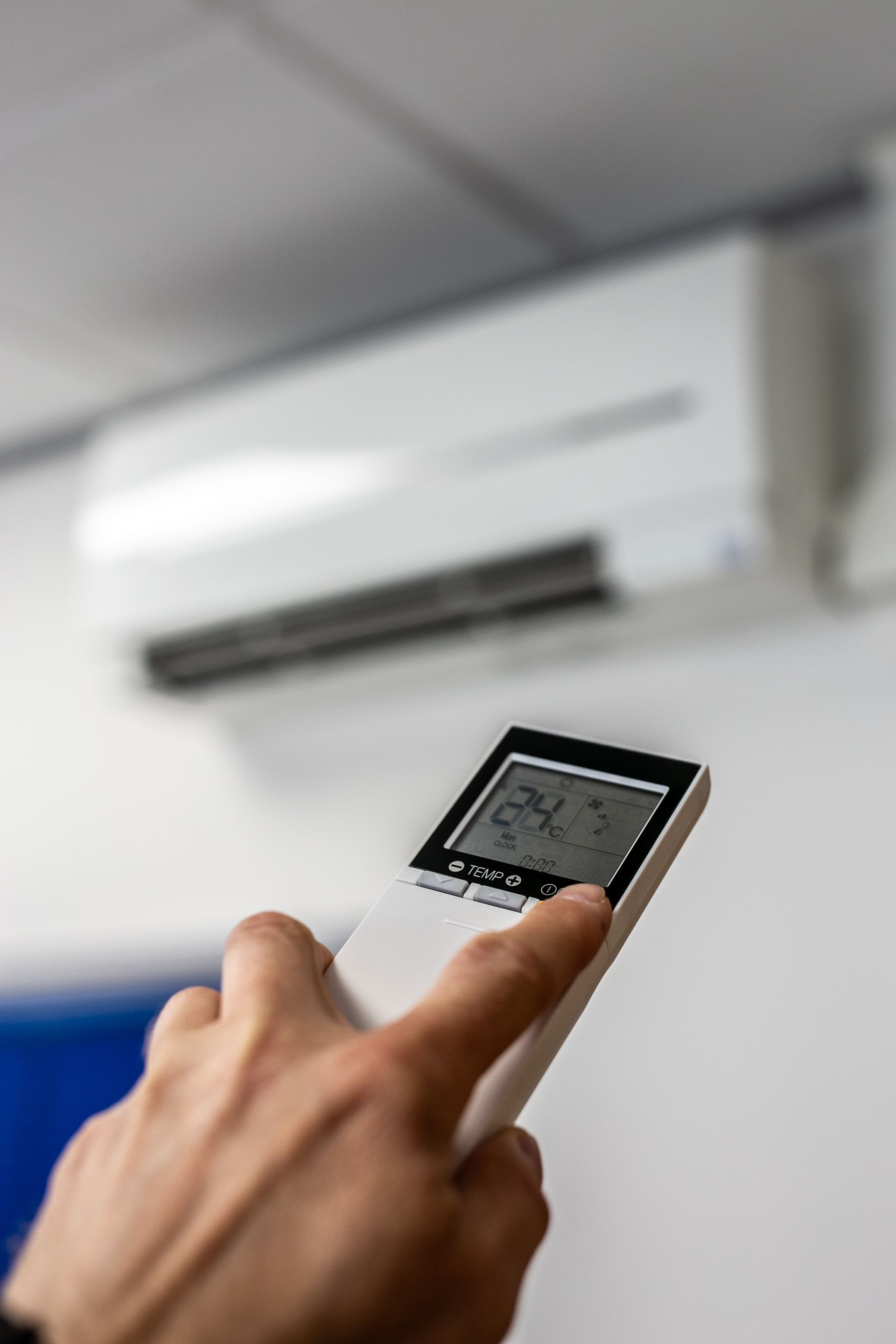Main tenant une télécommande pointée vers un climatiseur mural dans une pièce