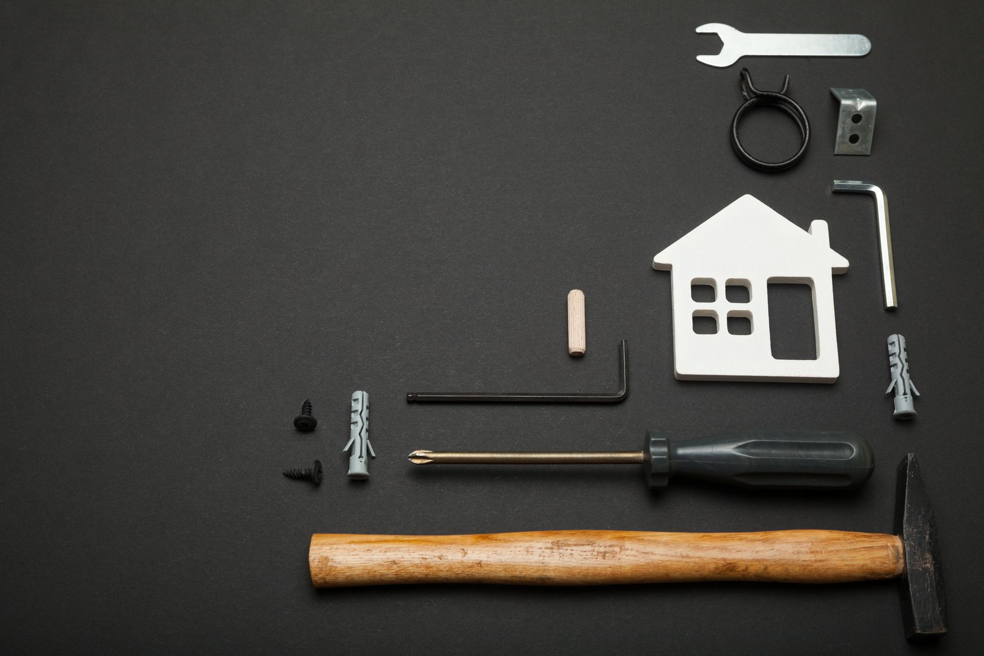 Des outils disposés autour d'une découpe de maison blanche sur une surface noire.