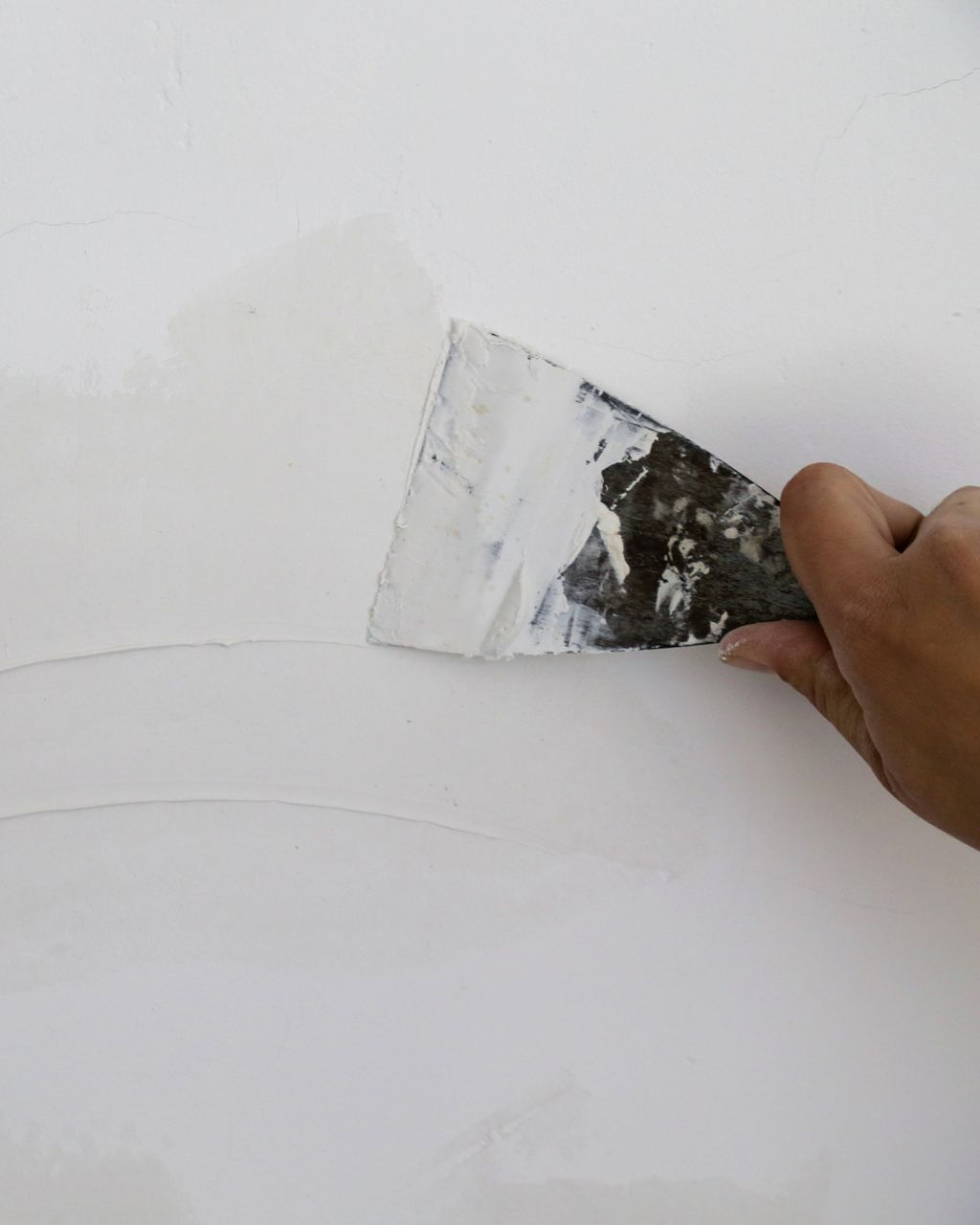 Main utilisant un couteau à mastic pour étaler de l'enduit blanc sur un mur blanc.