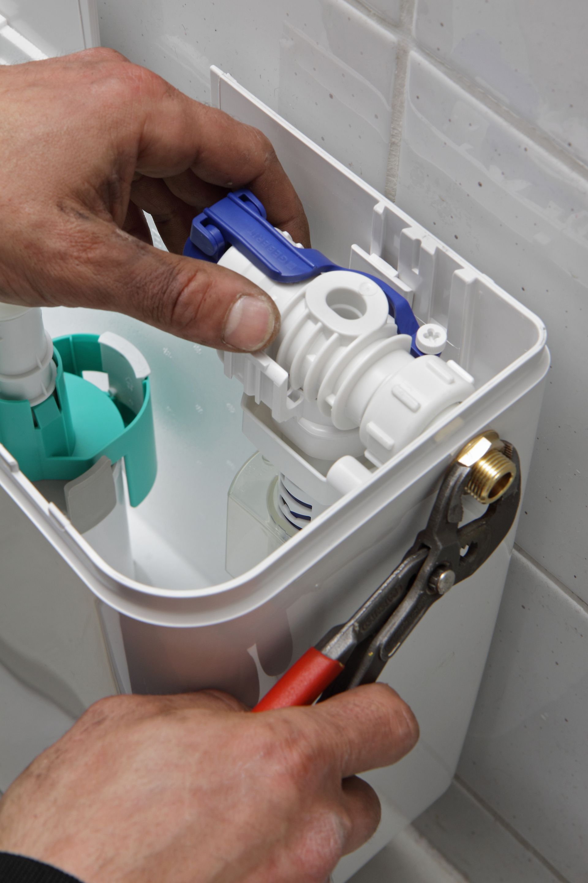 Des mains ajustent le robinet de remplissage des toilettes avec une pince à l'intérieur du réservoir.