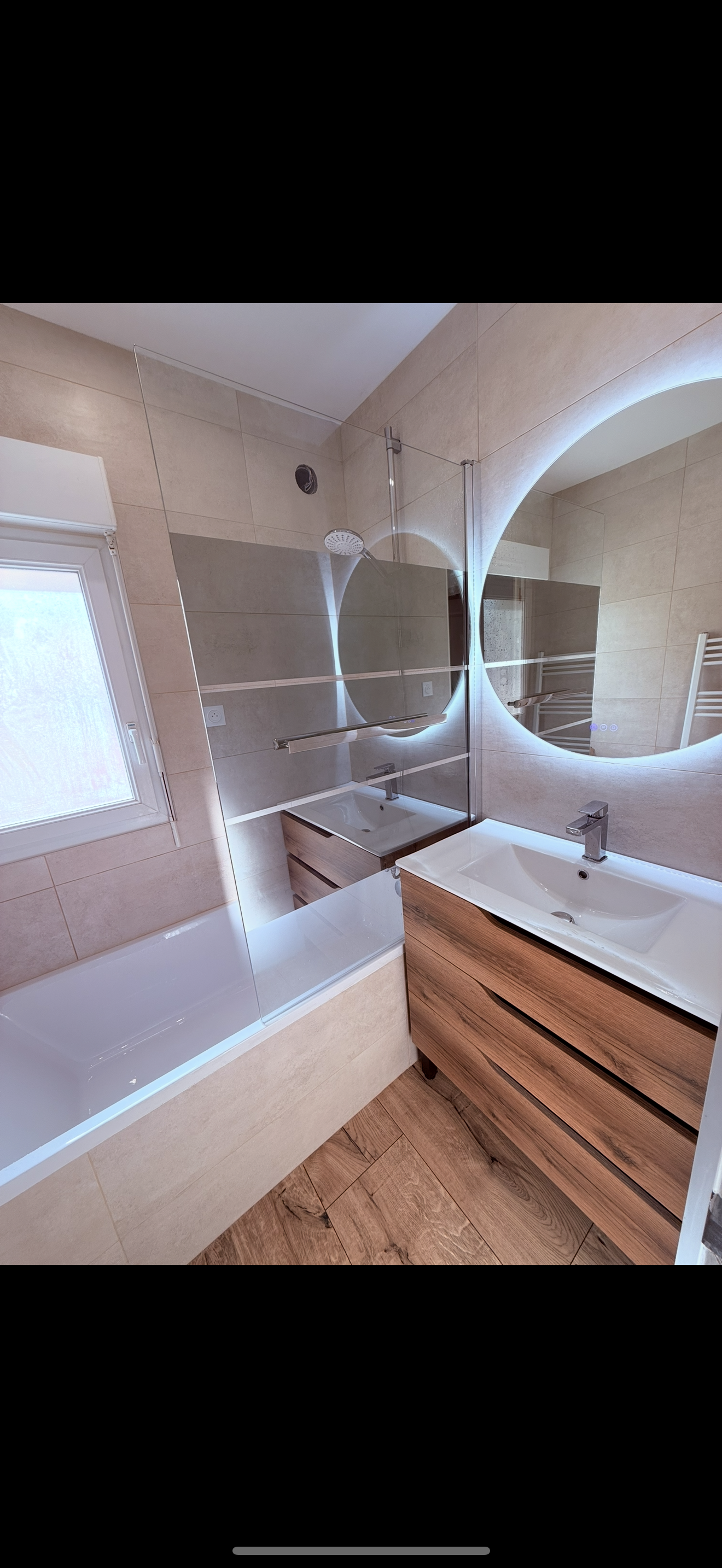 Salle de bains moderne avec meuble-lavabo en bois, miroir rond avec éclairage et baignoire.