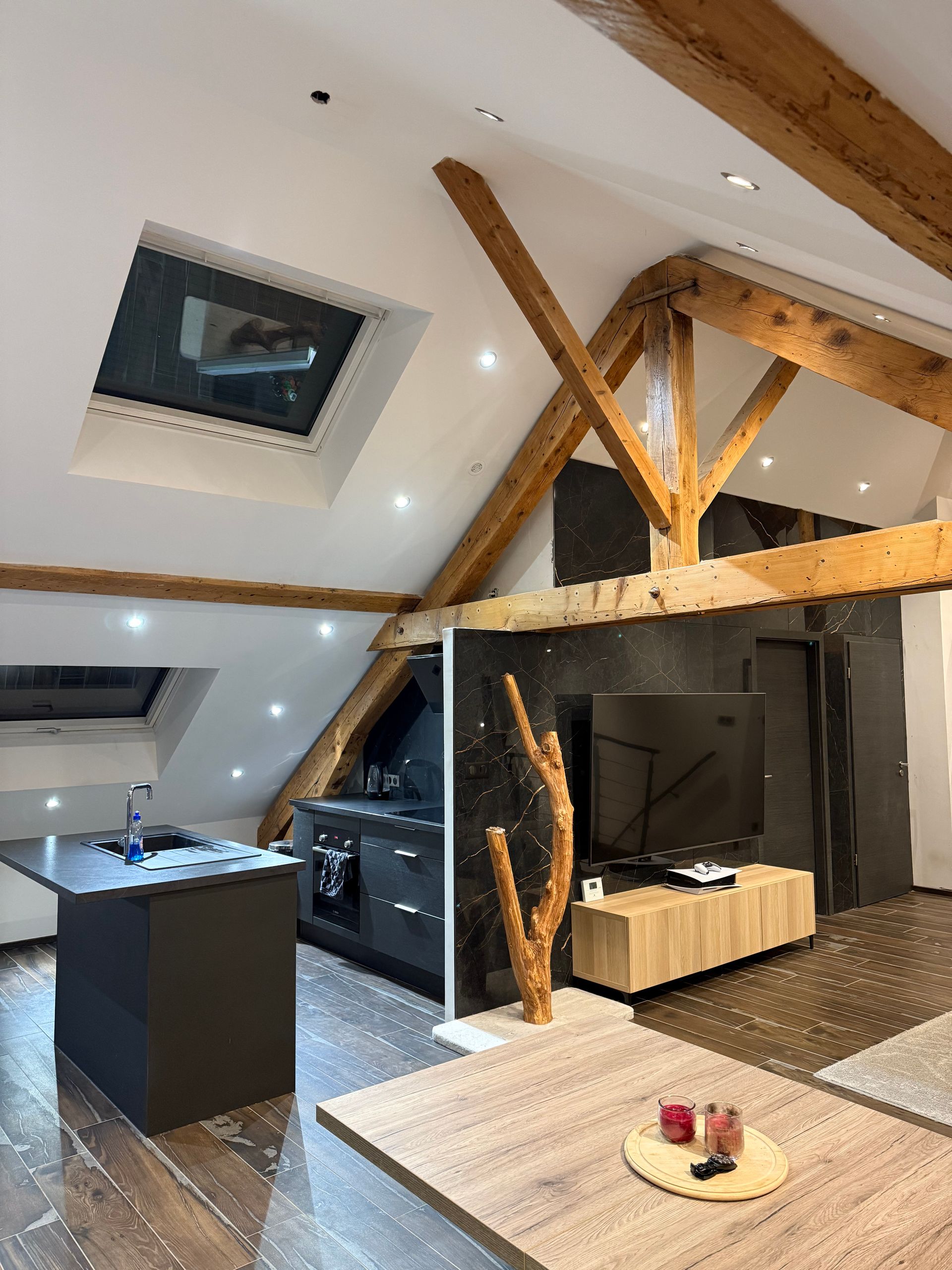 Cuisine moderne avec poutres apparentes, puits de lumière et meubles de cuisine foncés.