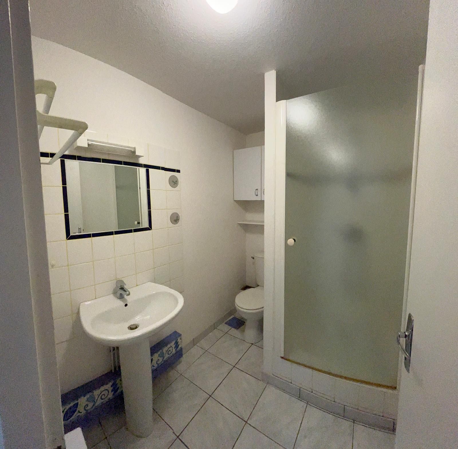 Salle de bains avec lavabo sur pied, douche, toilettes et carrelage blanc.