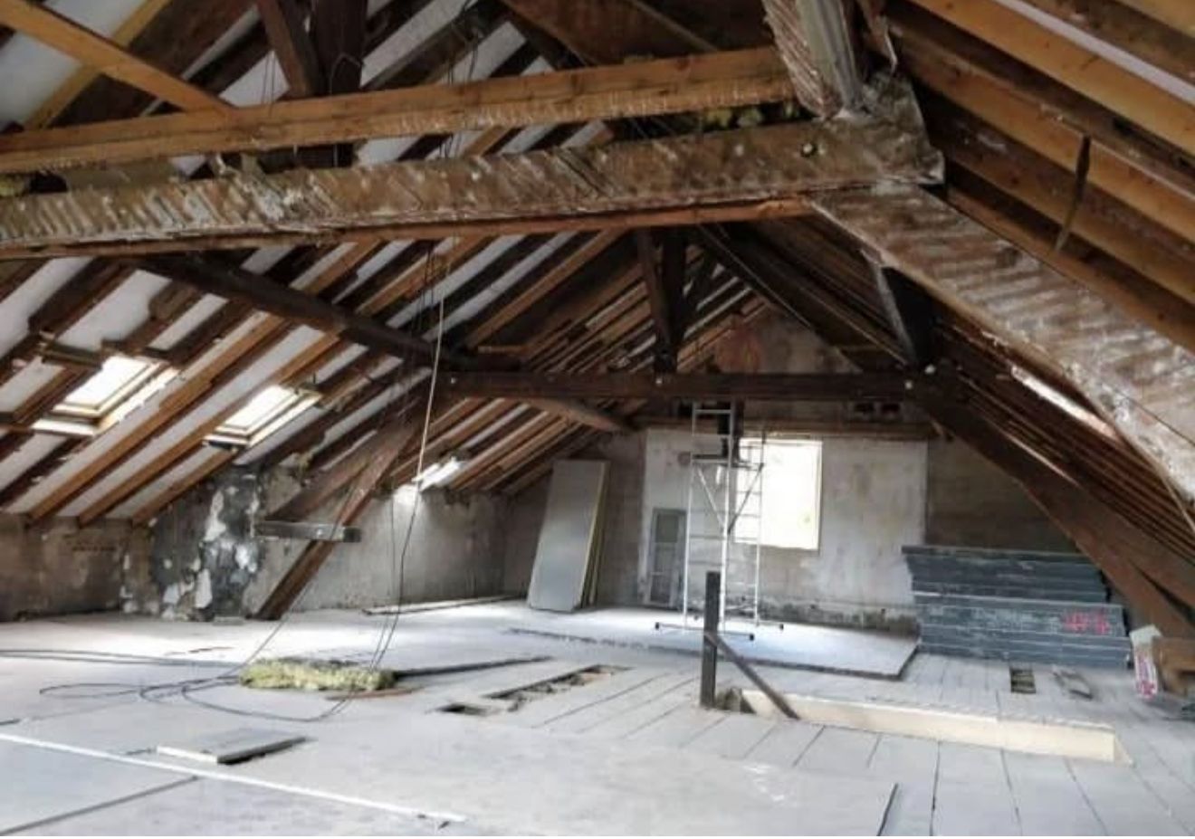 Vue intérieure d'un grenier en construction, avec poutres en bois apparentes, lumière naturelle et matériaux de construction.