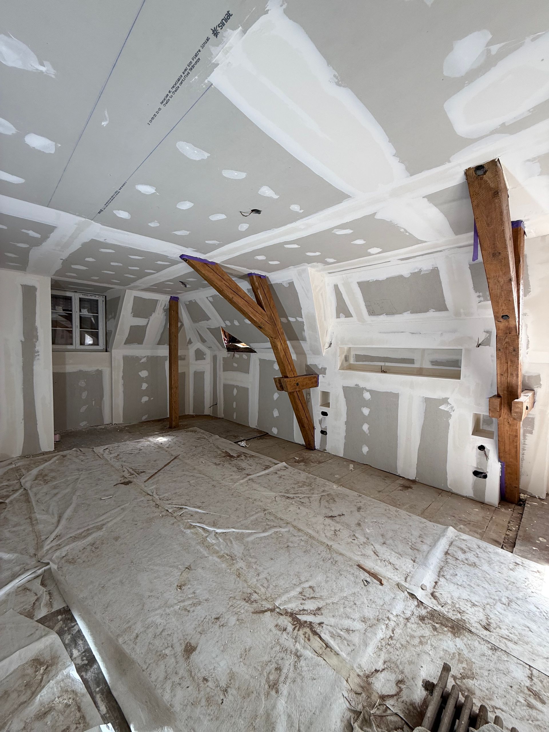 Pièce en travaux avec poutres apparentes, cloisons sèches et revêtement de sol protecteur.