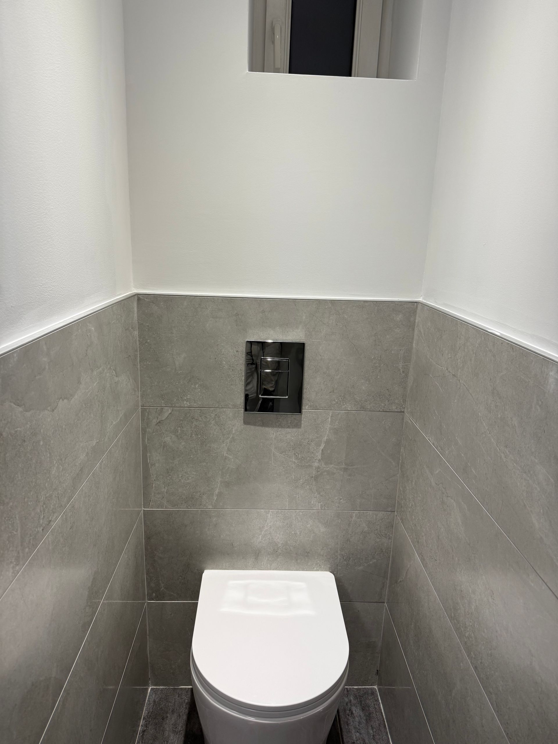 Une personne portant des gants bleus pose du carrelage mural. On aperçoit des carreaux beiges, de la colle beige clair et des croisillons orange.