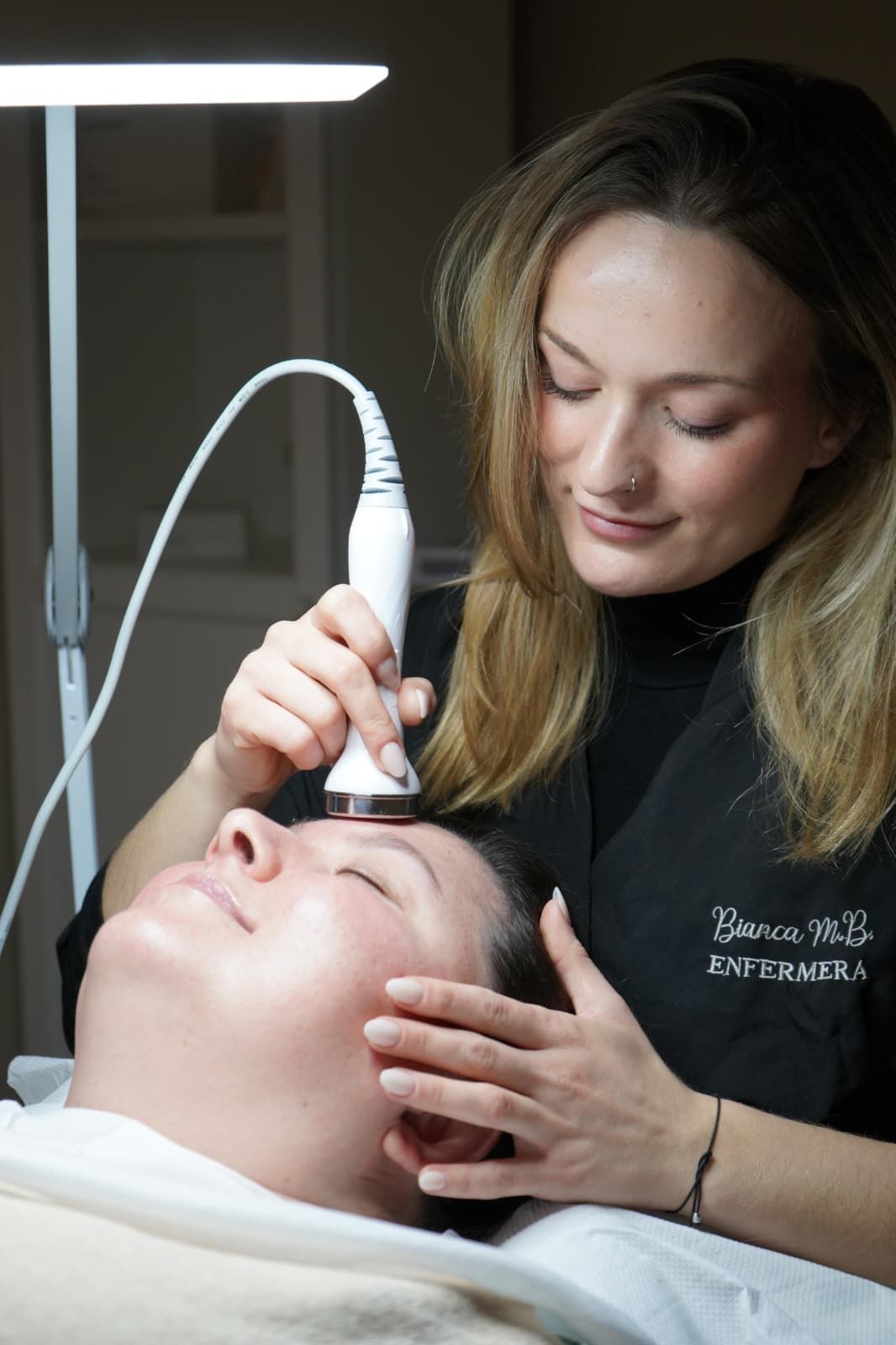 Una mujer realiza un tratamiento facial a un cliente con un dispositivo portátil.
