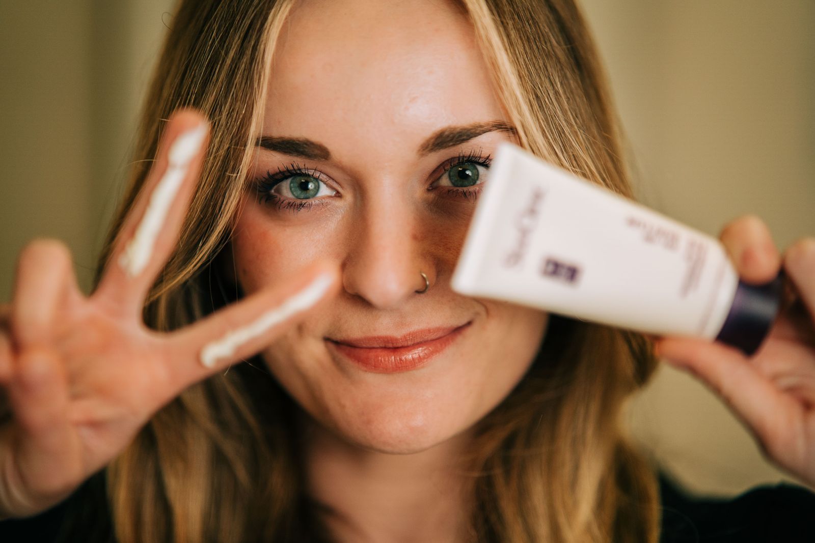 Mujer sosteniendo un producto para el cuidado de la piel, crema en los dedos en señal de paz.