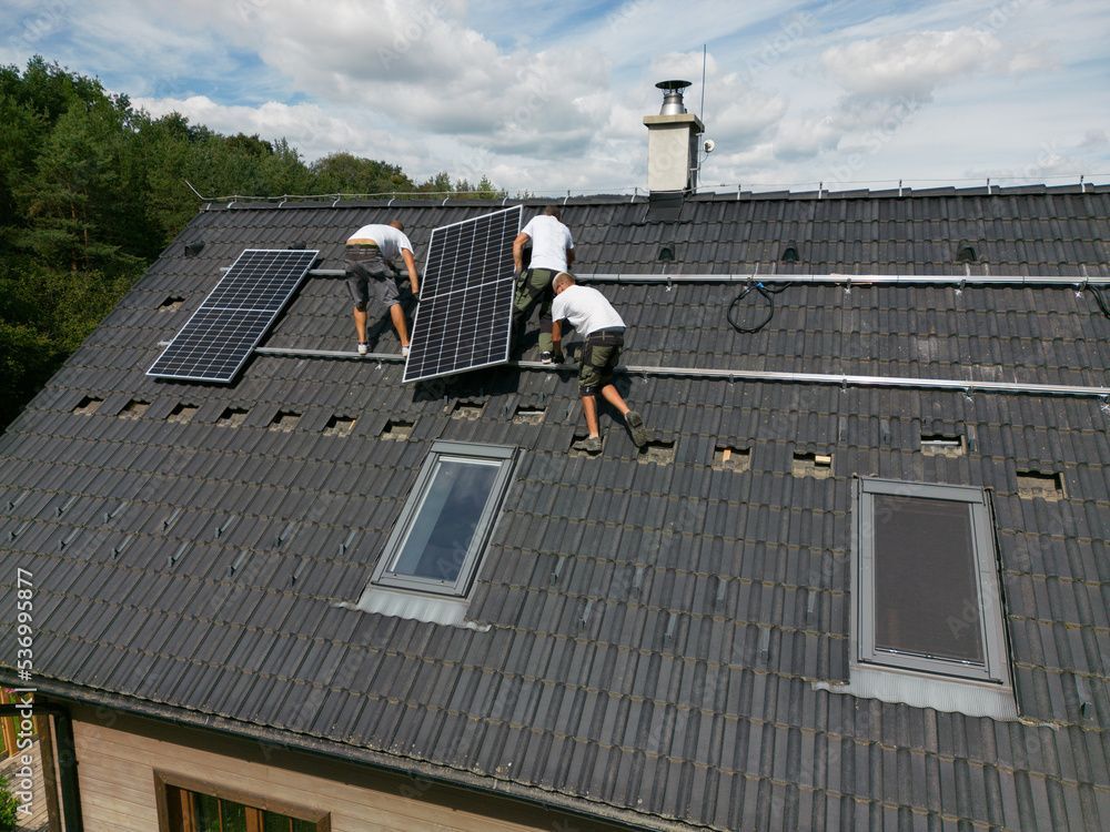 Trois hommes mettent en place des panneaux photovoltaïques sur une toiture