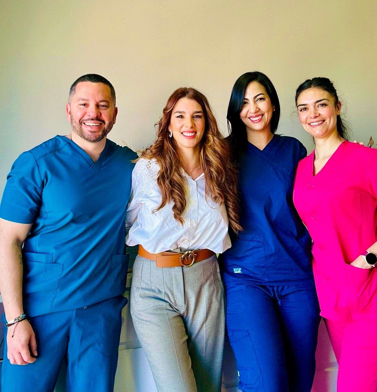 Cuatro personas de pie muy juntas; dos con batas médicas, una con blusa blanca y otra con blusa rosa.