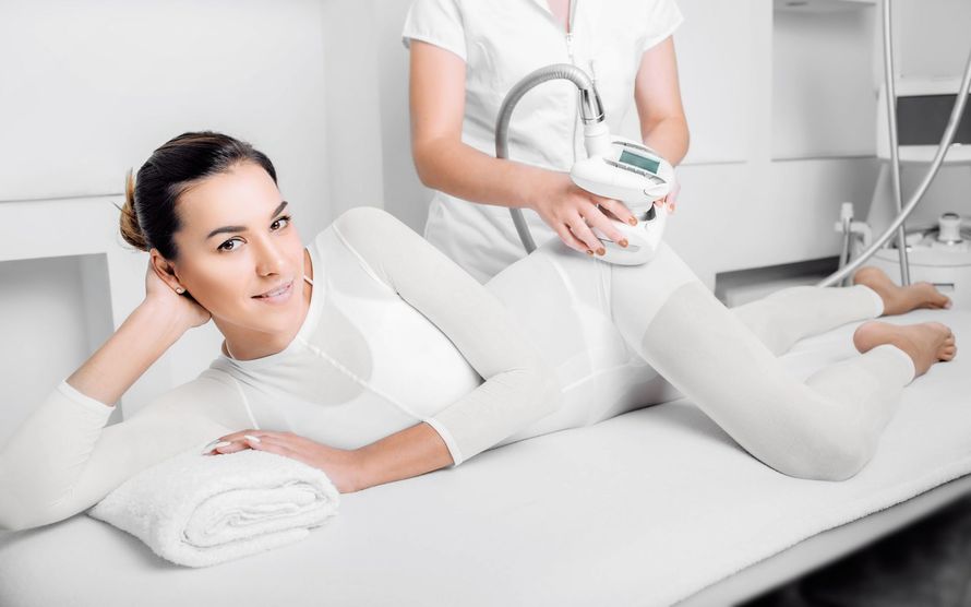 Mujer recibiendo un tratamiento de contorno corporal, acostada en una mesa, vistiendo un body.