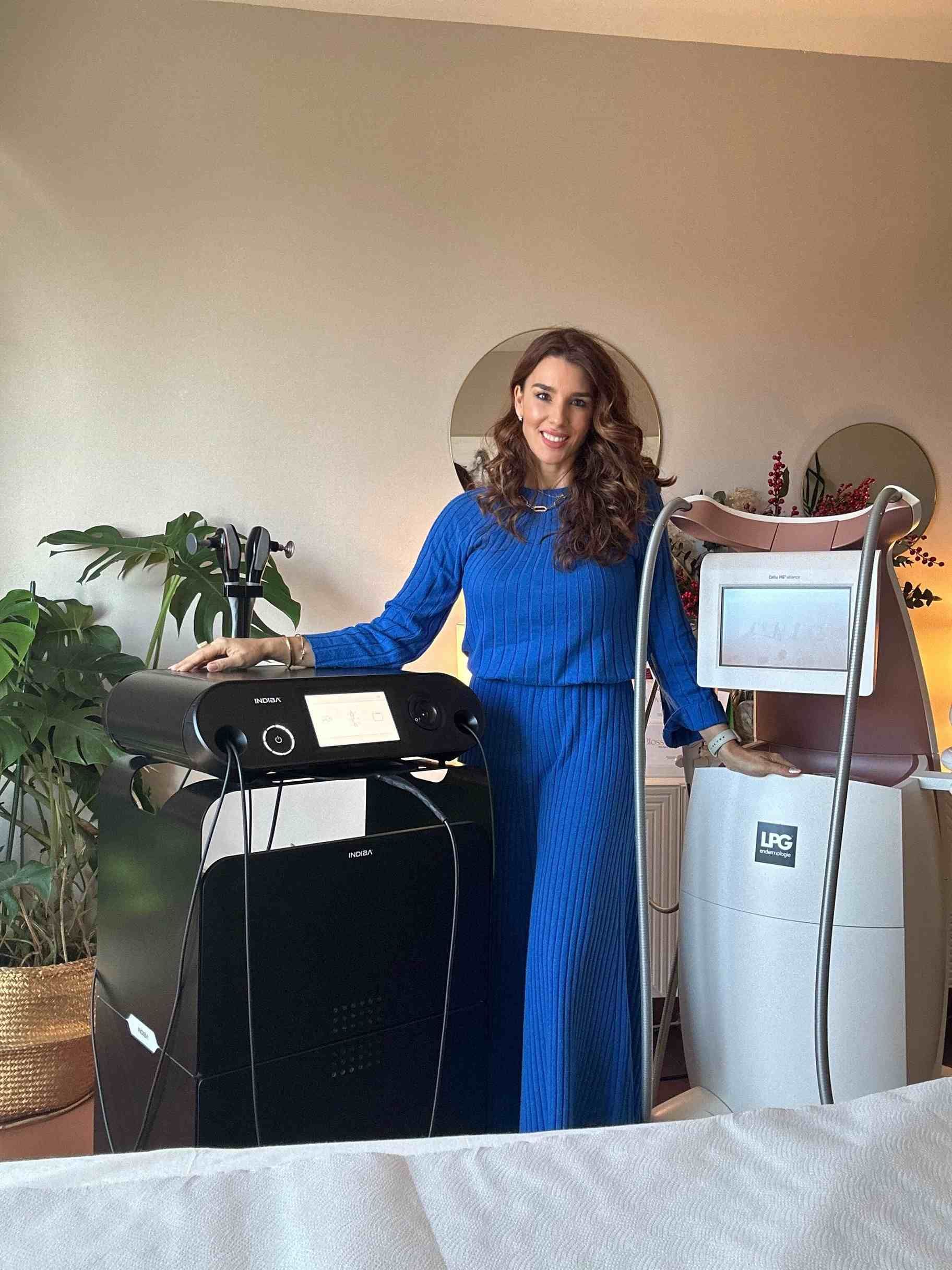 Una mujer vestida de azul está de pie junto a dos dispositivos médicos en una habitación.