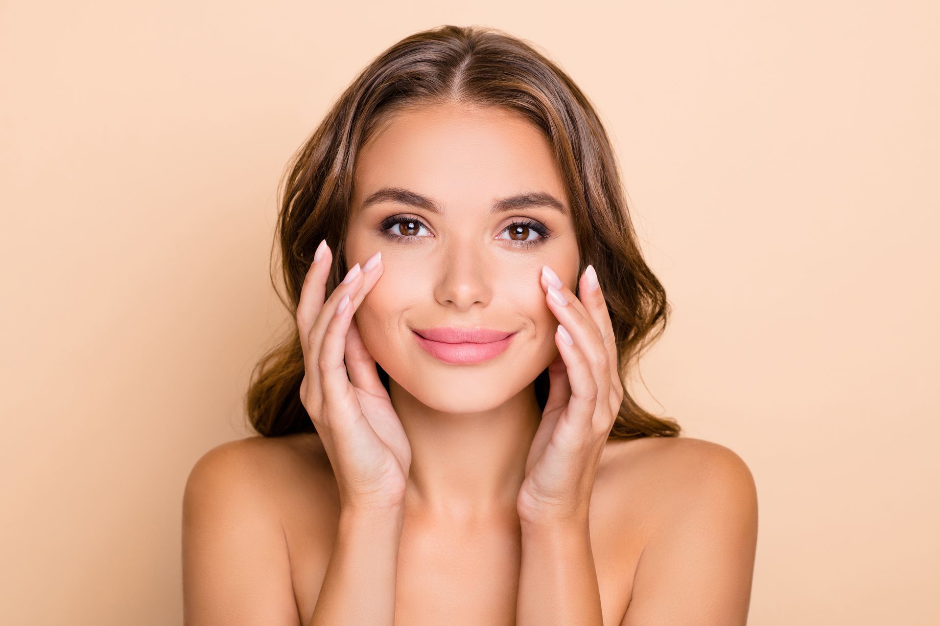 Una mujer sonríe, tocándose los ojos con ambas manos. Fondo color crema.