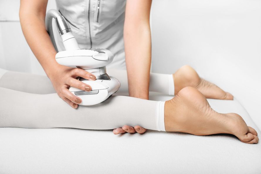 Persona que administra un tratamiento de piernas con un dispositivo portátil a un cliente en un spa.