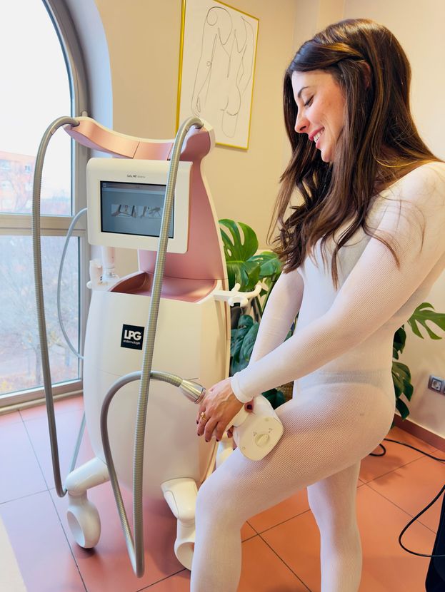 Mujer con traje de baño usando una máquina rosa de modelado corporal; sonriendo. Interior.