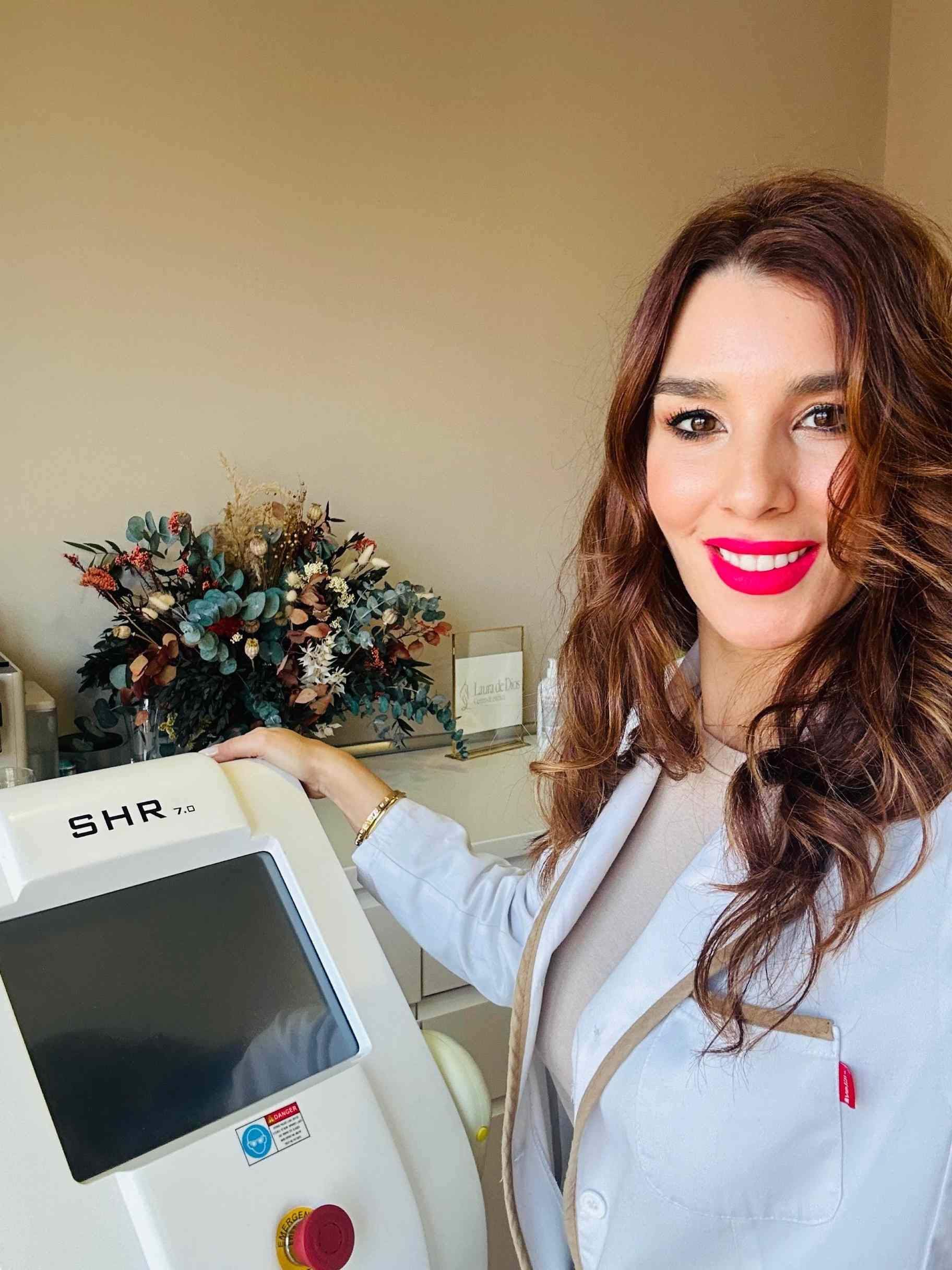 Mujer con bata de laboratorio y máquina de peinar, sonriendo en un entorno clínico.
