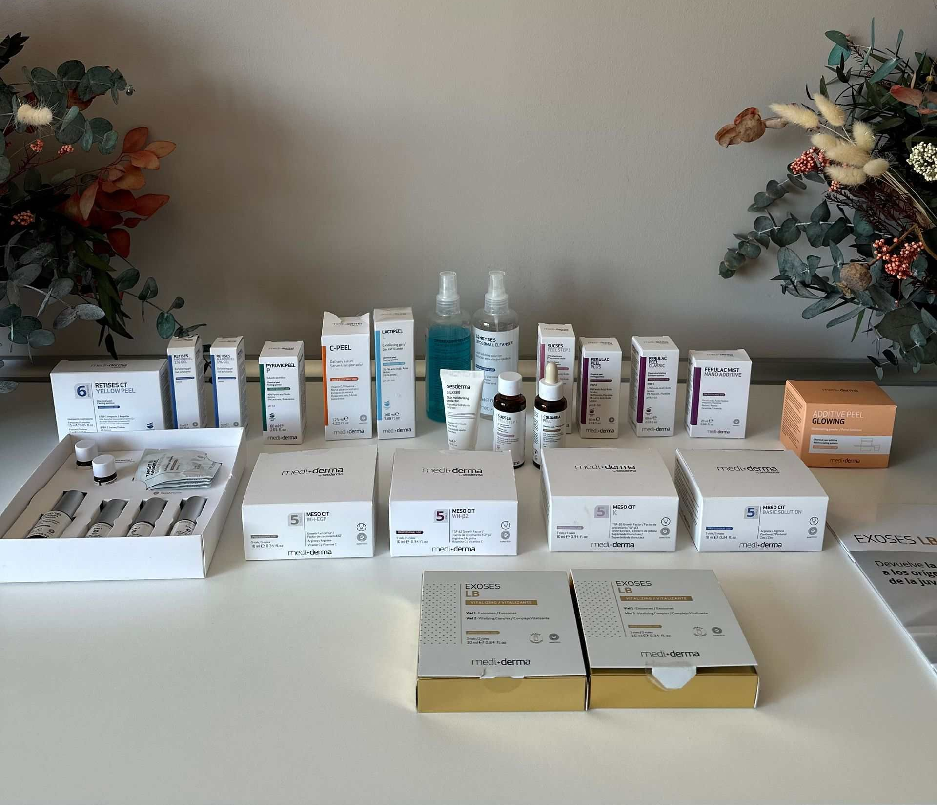 Diversos productos para el cuidado de la piel dispuestos sobre una superficie blanca con decoraciones florales de fondo.