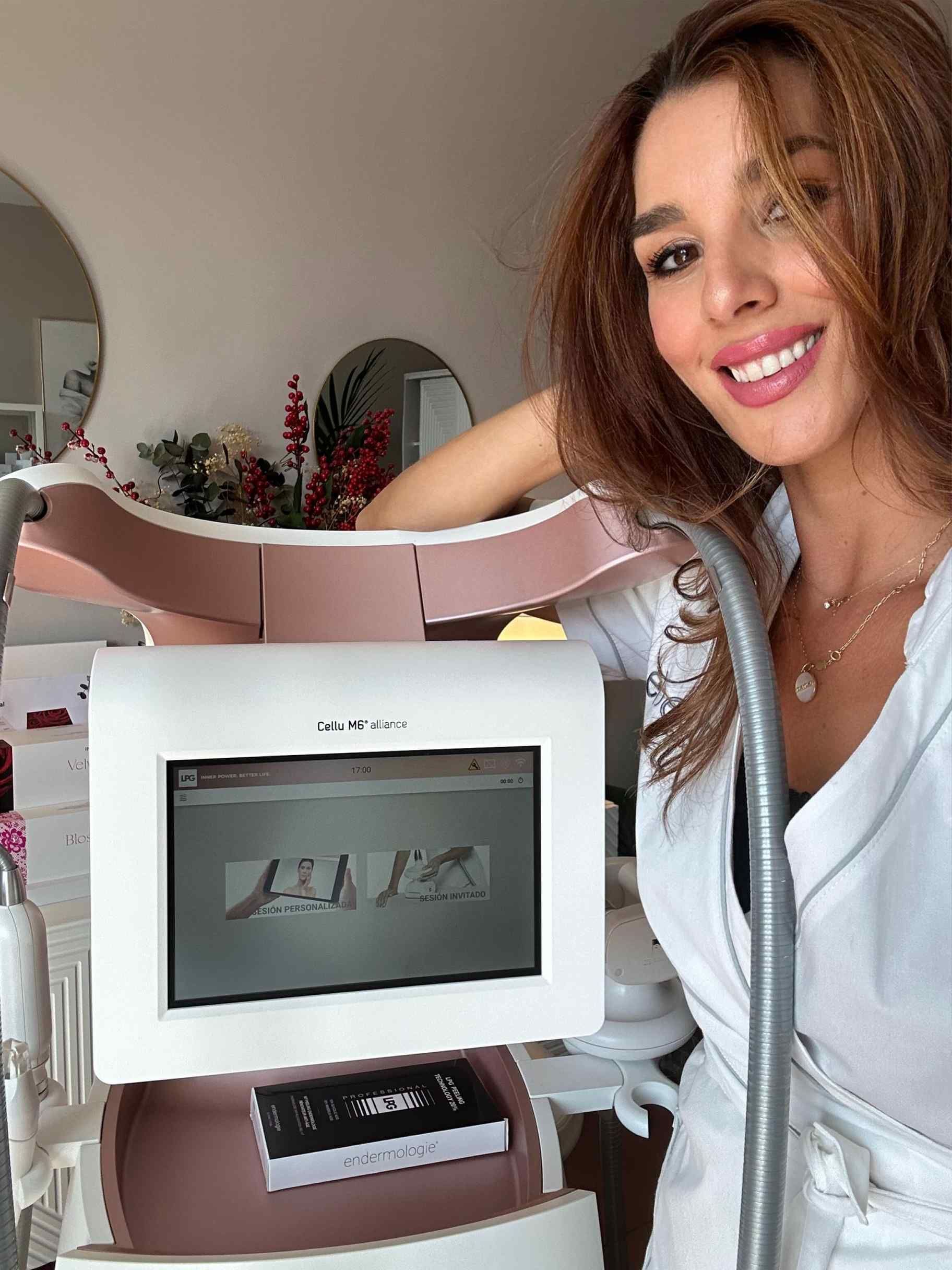 Mujer sonriendo cerca de un dispositivo médico con una pantalla que muestra texto en una habitación iluminada.