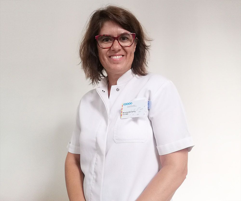 Mujer con bata blanca, gafas, sonriendo; en el interior, etiqueta con nombre visible.