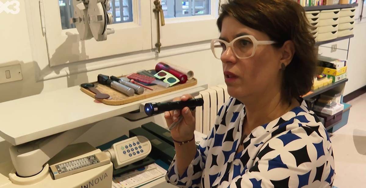 Mujer con gafas sosteniendo una linterna, mirándola en un entorno de oficina.