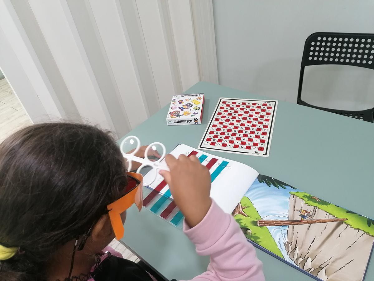 Una persona que usa gafas especiales examina un patrón colorido, parte de una actividad de aprendizaje con patrones sobre una mesa.