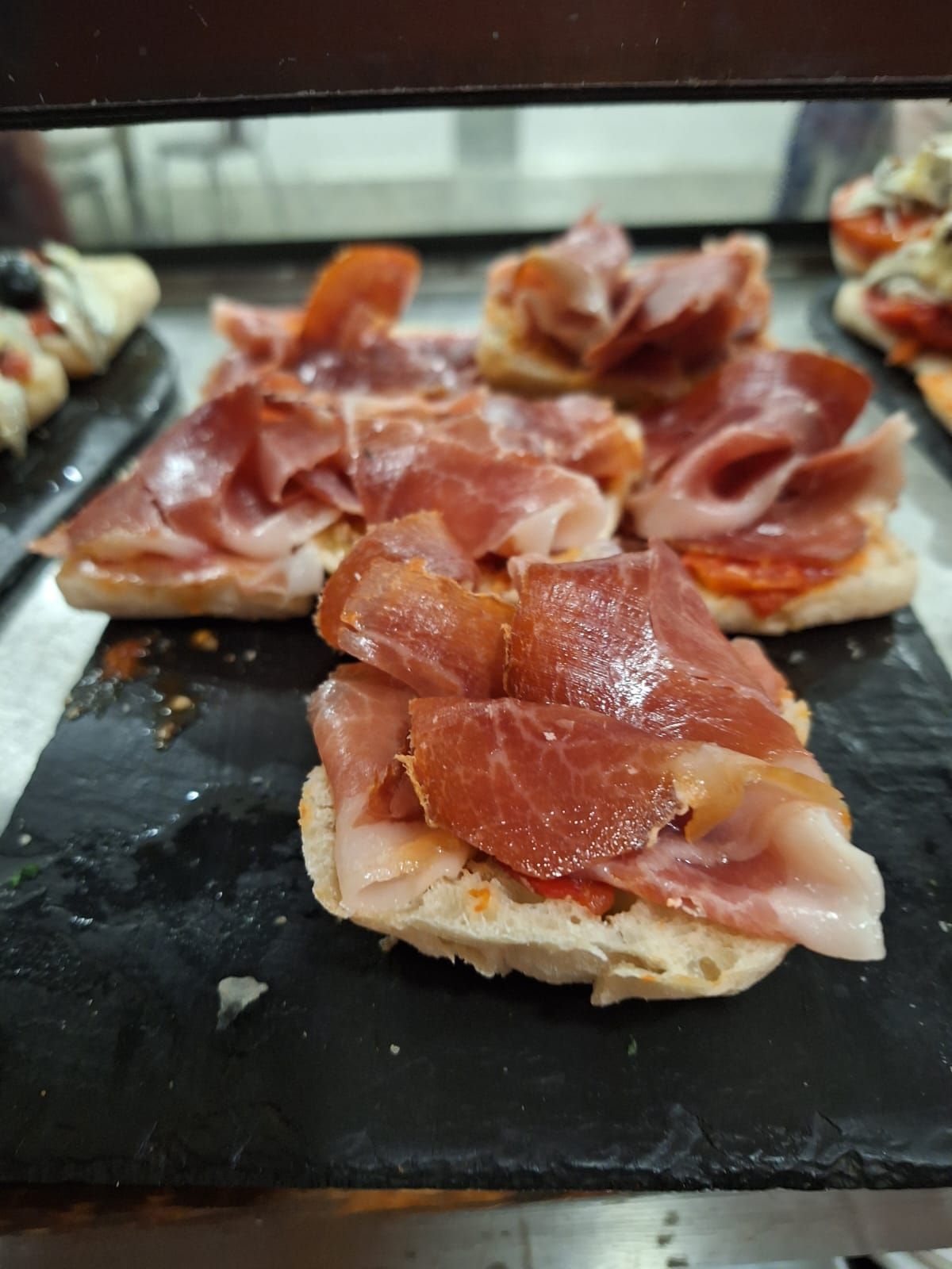 Sándwiches abiertos cubiertos con jamón curado y tomate en una bandeja de servir negra.