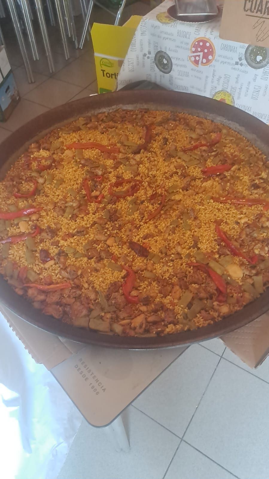 Paella en sartén redonda de color marrón, con pimientos rojos y arroz amarillo.
