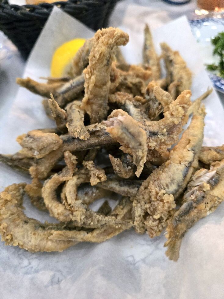 Montón de pequeños pescados empanizados y fritos con rodajas de limón, sobre papel pergamino.