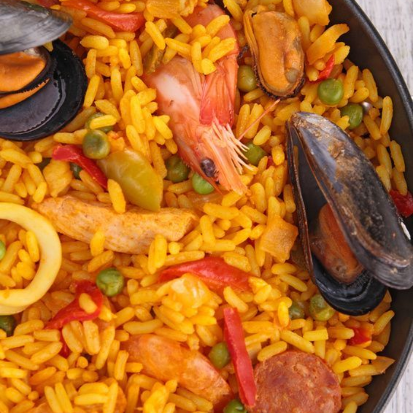 Paella con camarones, mejillones, guisantes, pimientos y calamares en un plato de arroz amarillo.